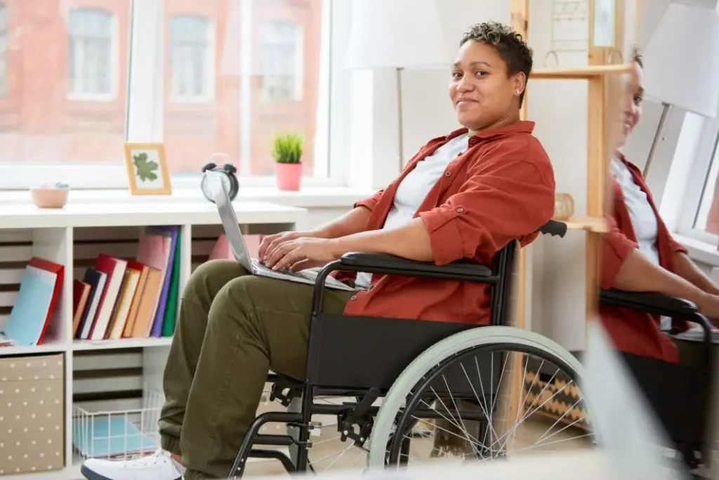 A young woman in a wheelchair working on her laptop.